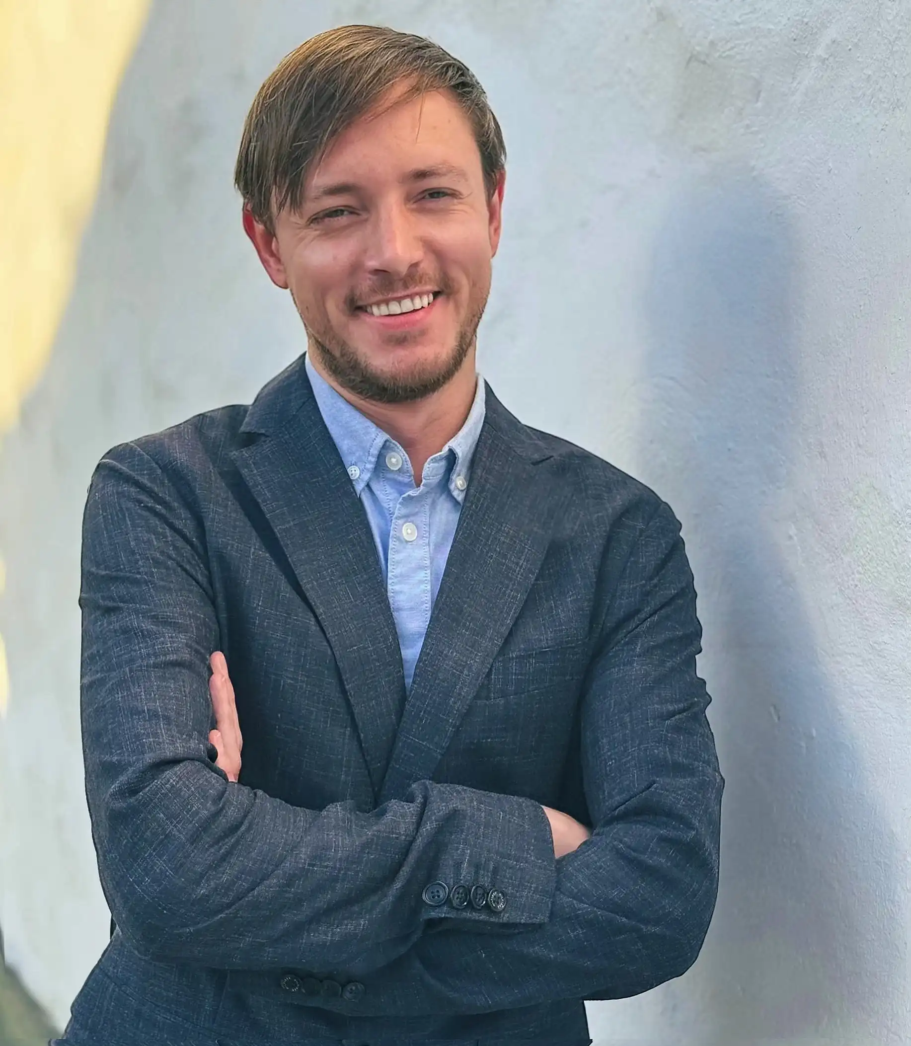 Markus Garth in einem blauen Sakko und Hemd, mit verschränkten Armen und einem freundlichen Lächeln vor einer weißen Wand.